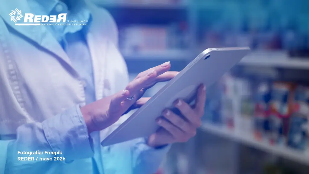 Farmacéutico utilizando tablet o computadora en mostrador de farmacia moderna con estantes de medicamentos al fondo.